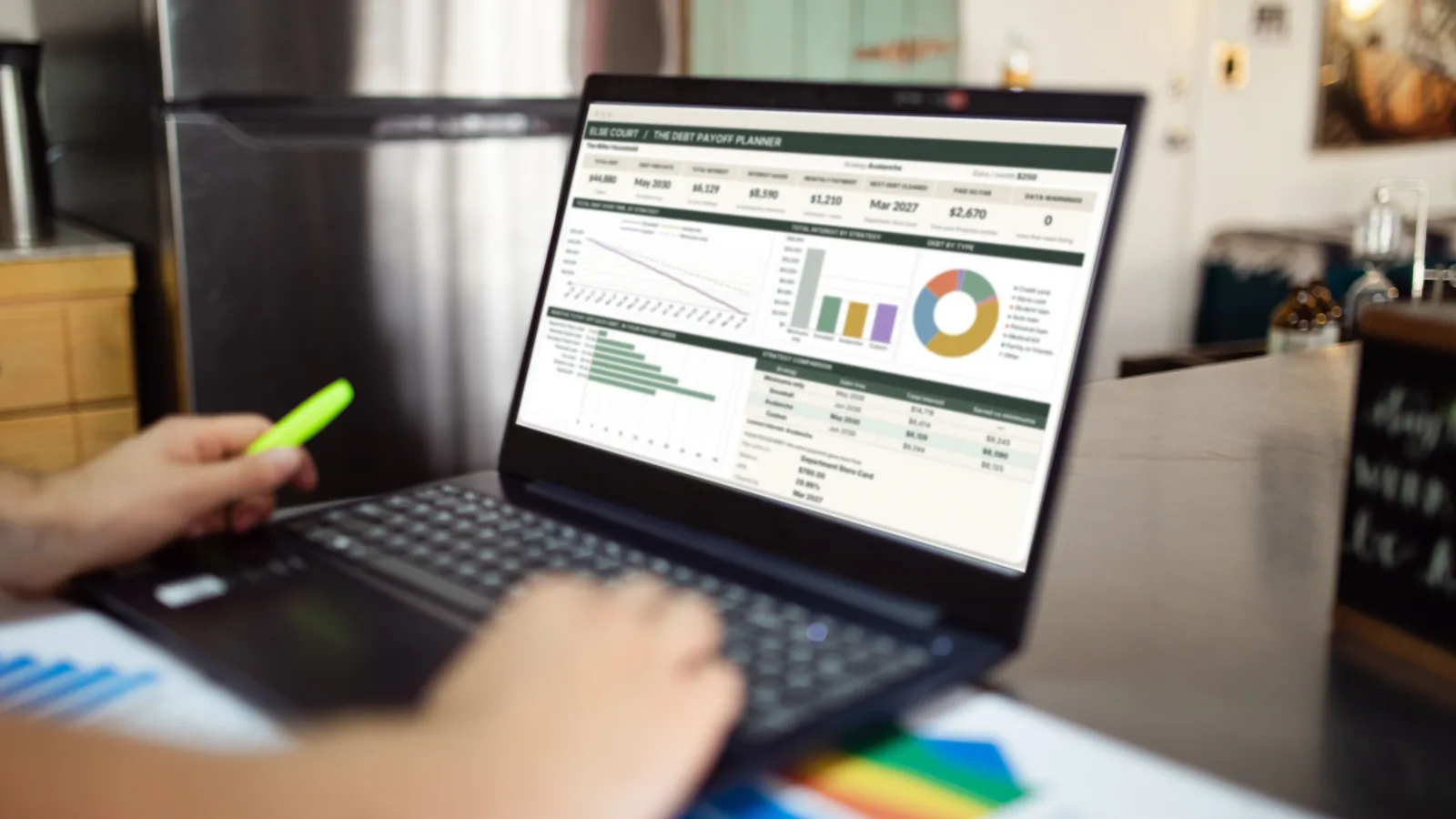 A person highlighting printed charts next to an open laptop that shows a debt payoff dashboard with a payoff timeline and a debt breakdown ring chart.